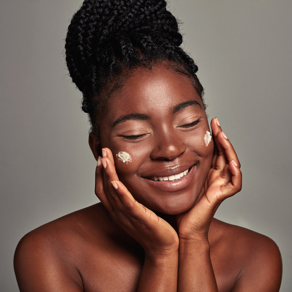 Studio shot of an attractive young woman applying moisturizer against a grey background