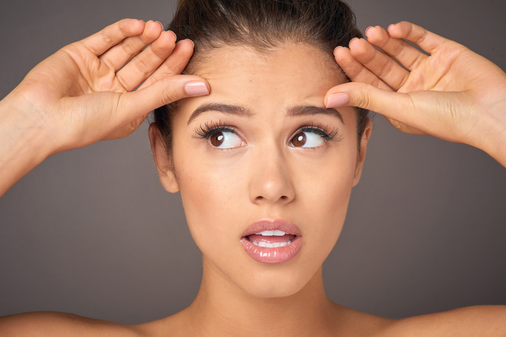 Studio portrait of a beautiful young woman concerned about forehead wrinkles against a gray background