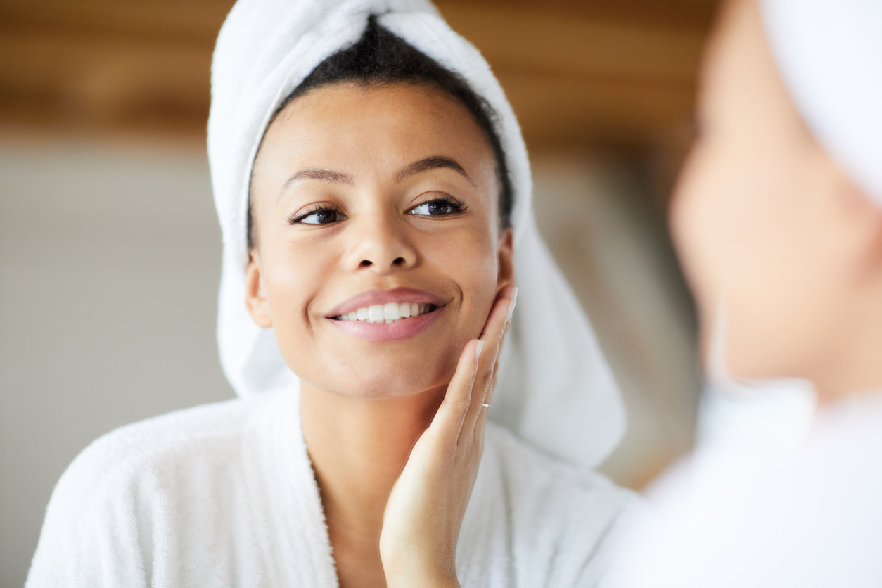 young woman with hair in a towel and bath robe smiling in the mirror